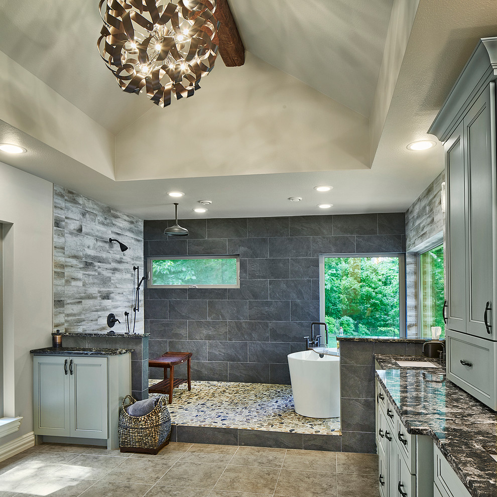 Photo of a large transitional master bathroom in Dallas with recessed-panel cabinets, grey cabinets, a freestanding tub, a curbless shower, gray tile, stone tile, beige walls, ceramic floors, a drop-in sink and granite benchtops.