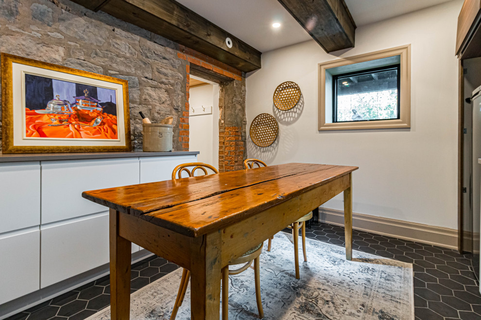 Mid-sized mountain style u-shaped ceramic tile, black floor and exposed beam eat-in kitchen photo in Toronto with a farmhouse sink, flat-panel cabinets, white cabinets, quartz countertops, white backsplash, subway tile backsplash, stainless steel appliances, an island and gray countertops