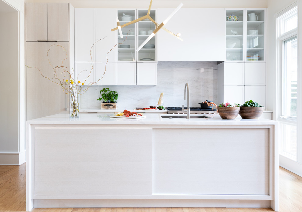 This is an example of a mid-sized midcentury single-wall kitchen pantry in DC Metro with an undermount sink, shaker cabinets, white cabinets, marble benchtops, white splashback, marble splashback, stainless steel appliances, light hardwood floors, with island, brown floor and white benchtop.