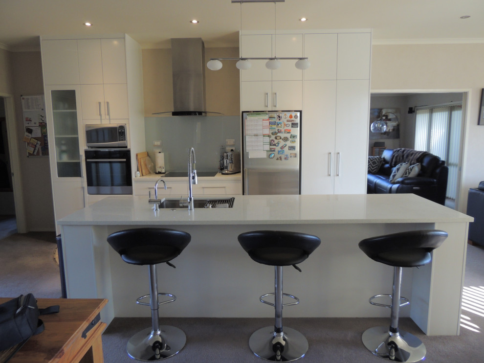 Mid-sized modern galley eat-in kitchen in Other with an undermount sink, flat-panel cabinets, white cabinets, quartz benchtops, metallic splashback, glass sheet splashback, with island and white benchtop.
