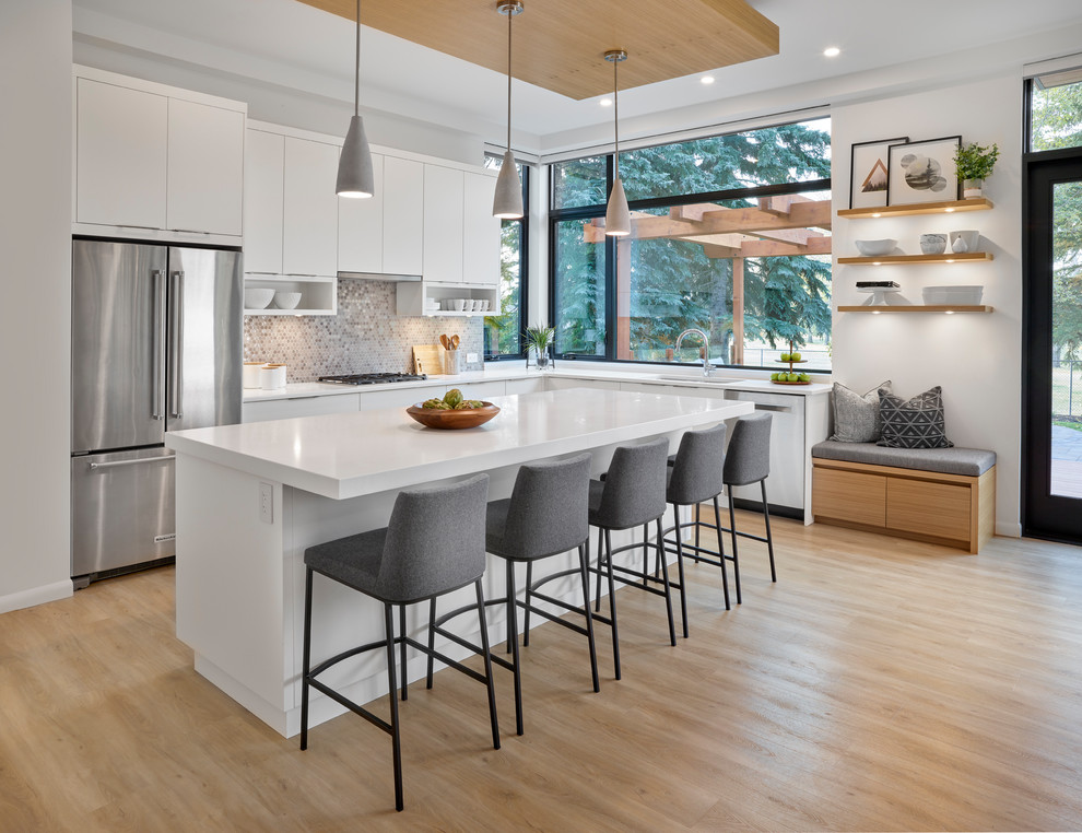 This is an example of a contemporary l-shaped kitchen in Edmonton with an undermount sink, flat-panel cabinets, white cabinets, metallic splashback, metal splashback, stainless steel appliances, light hardwood floors, with island and white benchtop.