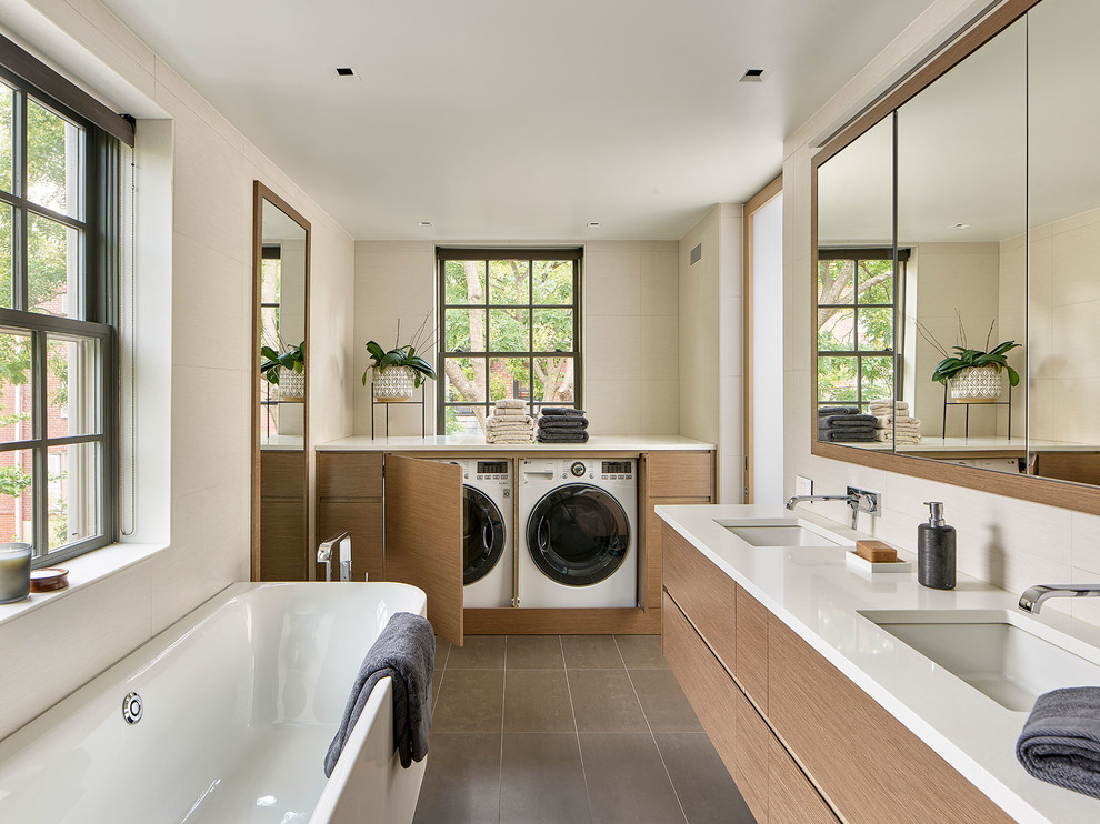 This is an example of a modern master bathroom in Philadelphia with flat-panel cabinets, medium wood cabinets, a freestanding tub, white walls, an undermount sink, grey floor, white benchtops, a wall-mount toilet, engineered quartz benchtops and a laundry.