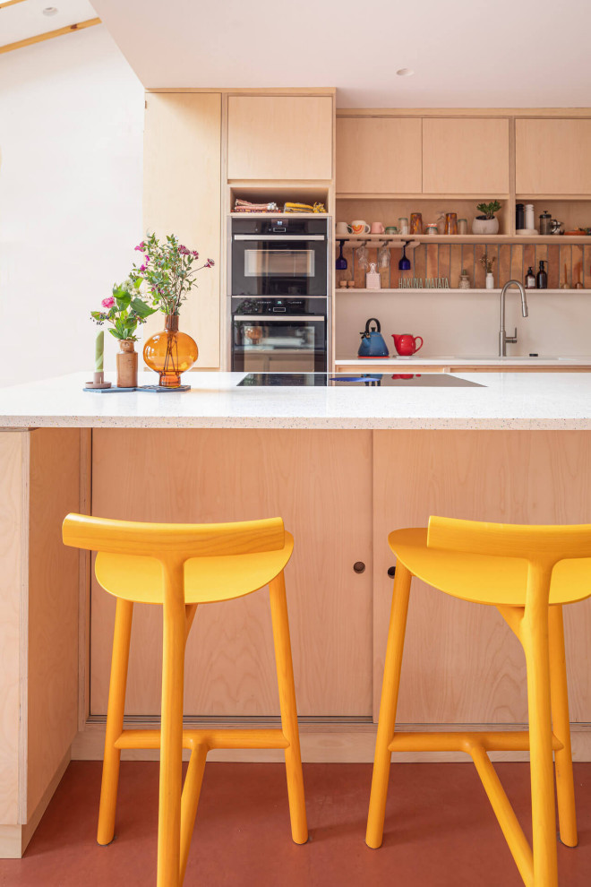 Example of a large trendy galley concrete floor and pink floor open concept kitchen design in Gloucestershire with flat-panel cabinets, light wood cabinets and an island