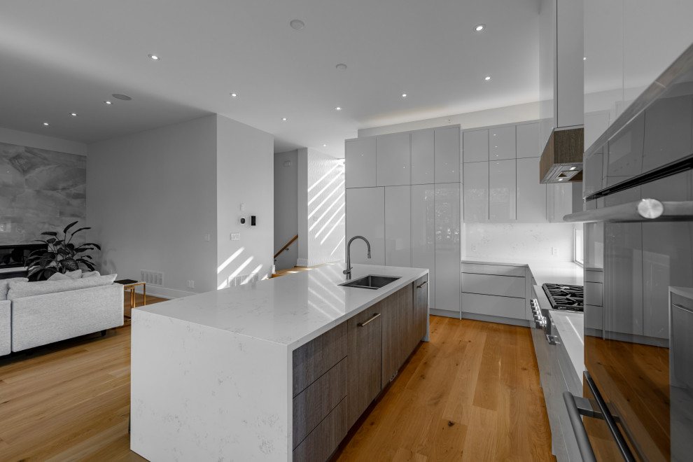 Idéer för ett stort modernt grå kök, med en enkel diskho, luckor med lamellpanel, grå skåp, granitbänkskiva, grått stänkskydd, rostfria vitvaror, en köksö och brunt golv