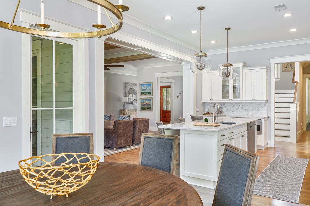 Photo of a large beach style u-shaped eat-in kitchen in Charleston with a drop-in sink, quartzite benchtops, white splashback, mosaic tile splashback, stainless steel appliances, medium hardwood floors, with island, brown floor, white cabinets and white benchtop.