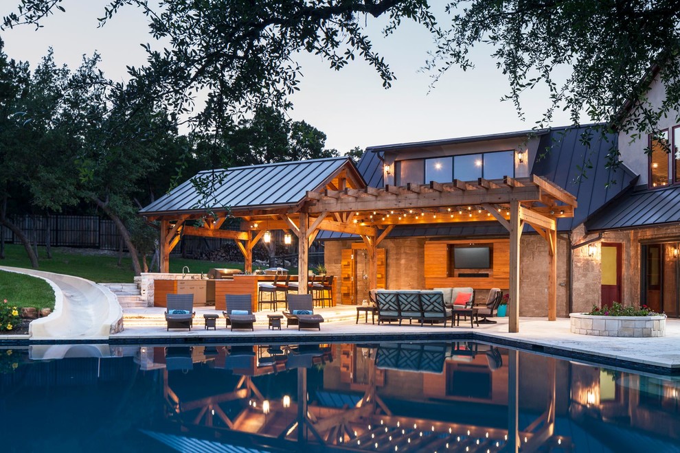 This is an example of an expansive transitional backyard deck in Austin with an outdoor kitchen and a roof extension.