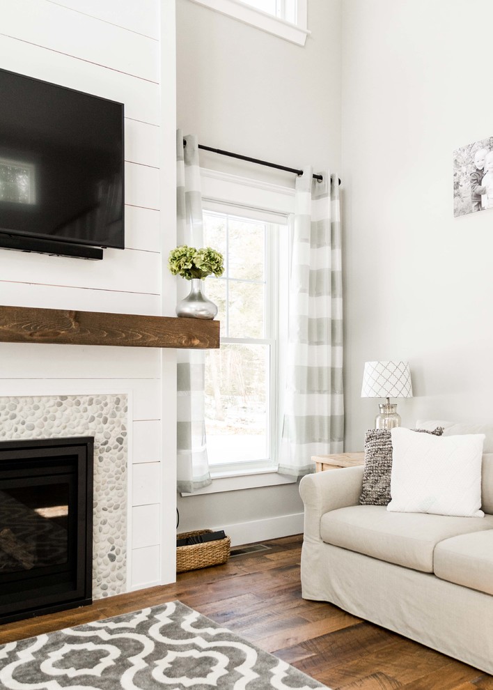Inspiration for a large farmhouse enclosed medium tone wood floor and brown floor living room remodel in Portland Maine with gray walls, a standard fireplace, a stone fireplace and a wall-mounted tv