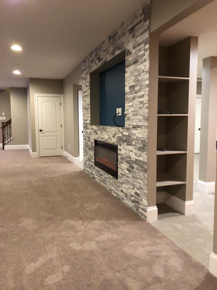 Large modern look-out basement with grey walls, carpet, a ribbon fireplace, a stone fireplace surround and beige floor.