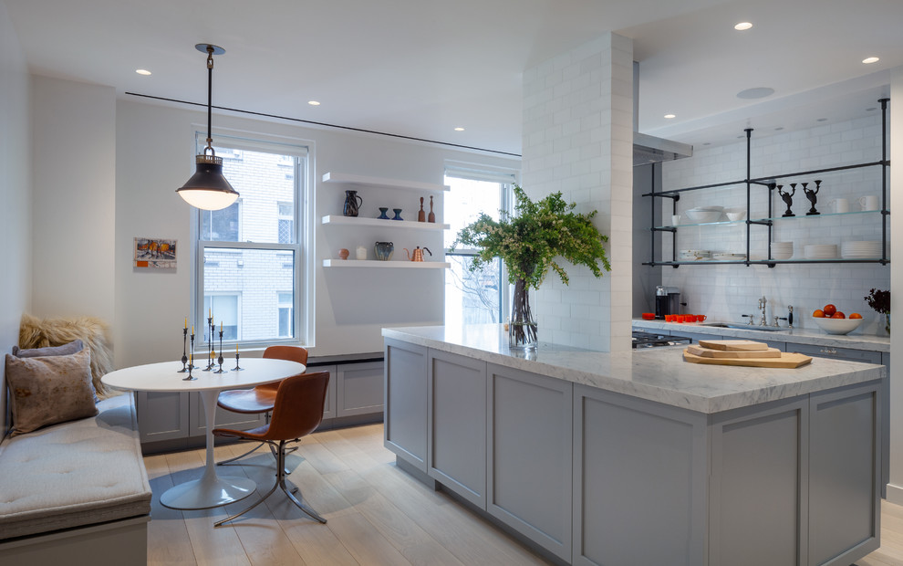 Example of a large transitional u-shaped light wood floor and beige floor eat-in kitchen design in New York with an undermount sink, shaker cabinets, gray cabinets, white backsplash, subway tile backsplash, an island, white countertops, marble countertops and stainless steel appliances
