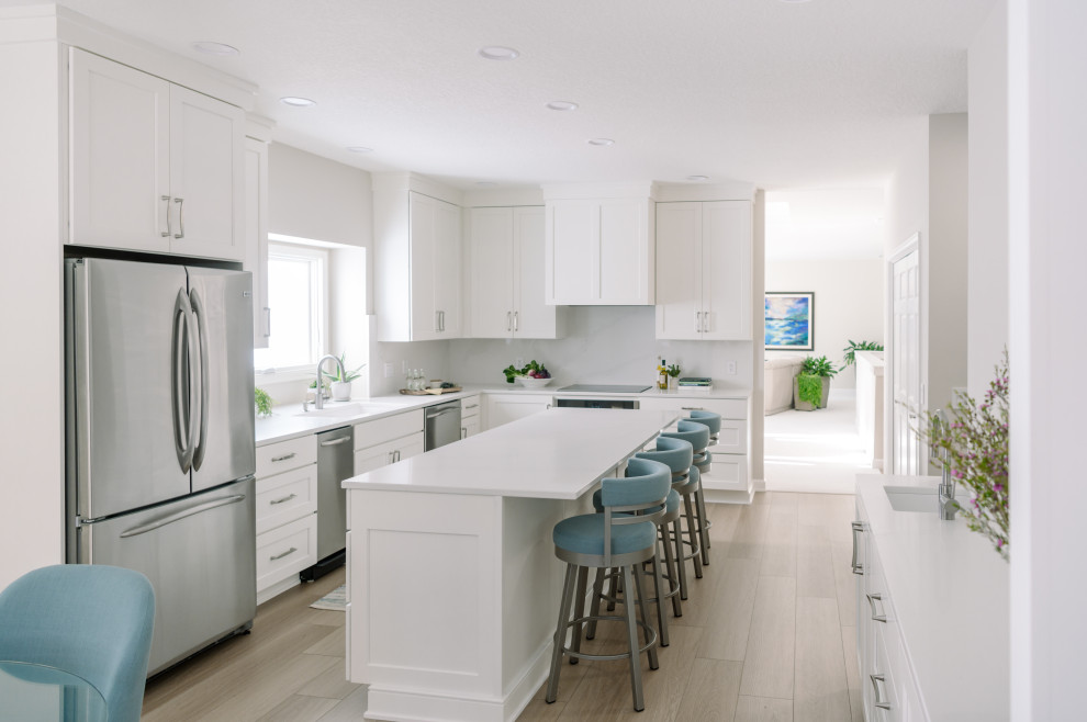 Inspiration for a large transitional l-shaped laminate floor and brown floor eat-in kitchen remodel with an undermount sink, shaker cabinets, white cabinets, quartz countertops, white backsplash, quartz backsplash, stainless steel appliances, an island and white countertops