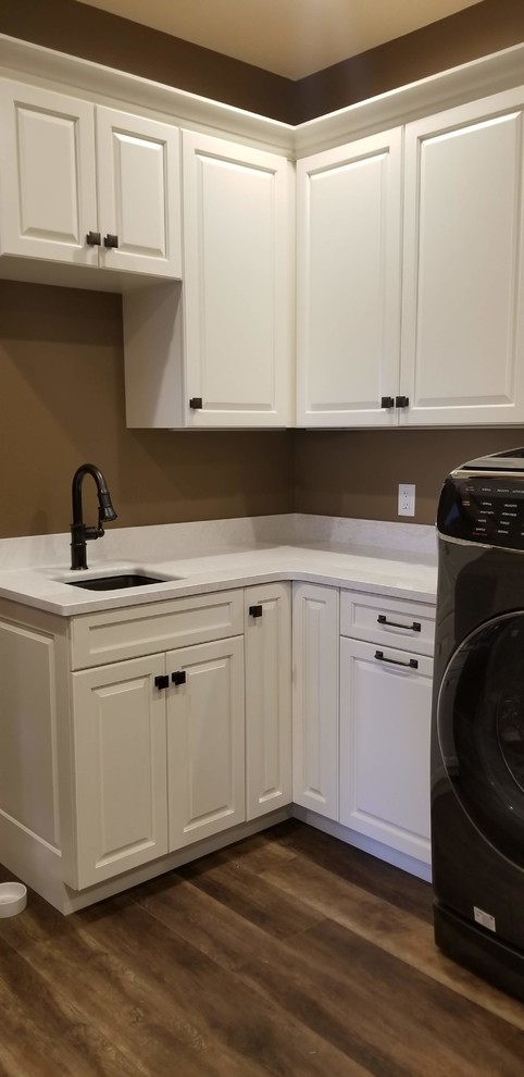 Photo of a large traditional u-shaped utility room in Cedar Rapids with an undermount sink, raised-panel cabinets, white cabinets, quartz benchtops, beige walls, medium hardwood floors, a side-by-side washer and dryer, brown floor and white benchtop.