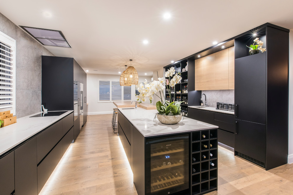 Photo of a large contemporary galley eat-in kitchen in Christchurch with an undermount sink, flat-panel cabinets, black cabinets, quartz benchtops, grey splashback, porcelain splashback, black appliances, light hardwood floors, with island and white benchtop.