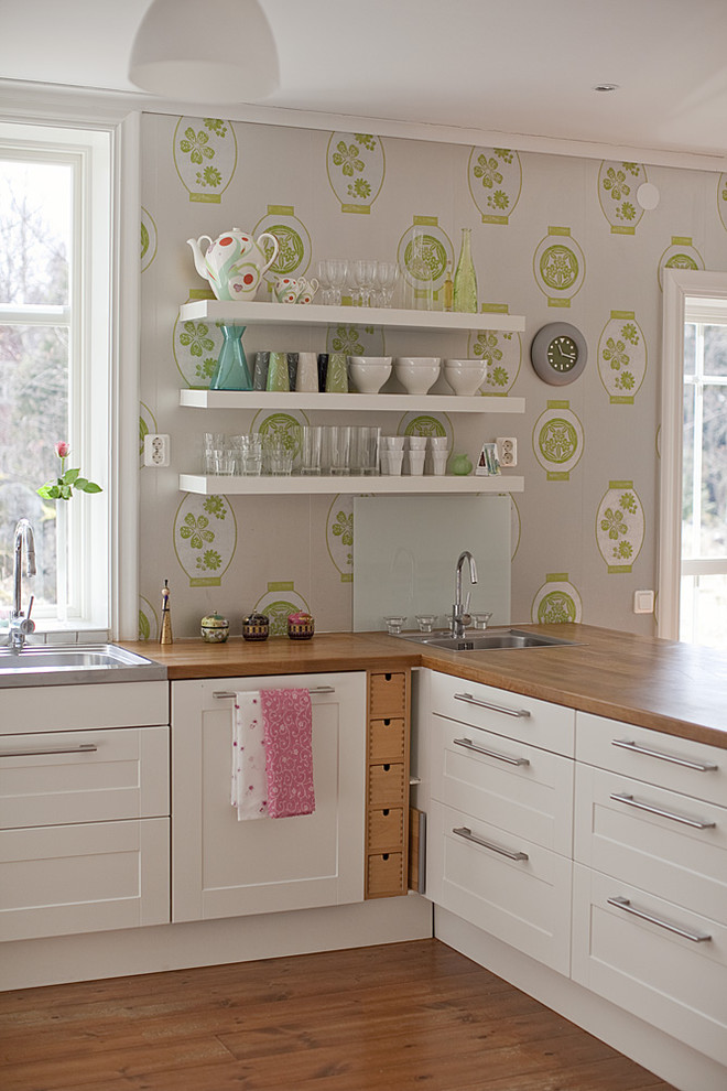 Mid-sized eclectic u-shaped eat-in kitchen in Stockholm with a double-bowl sink, white cabinets, wood benchtops, stainless steel appliances, medium hardwood floors, no island and recessed-panel cabinets.