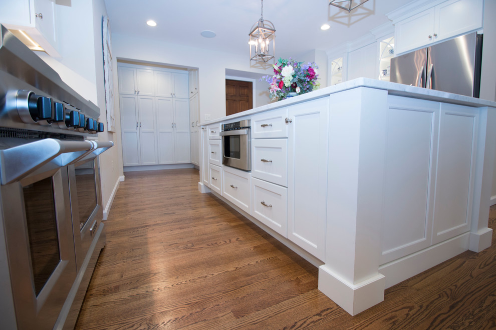 Huge transitional medium tone wood floor open concept kitchen photo with an undermount sink, shaker cabinets, white cabinets, marble countertops, white backsplash, ceramic backsplash, stainless steel appliances and two islands