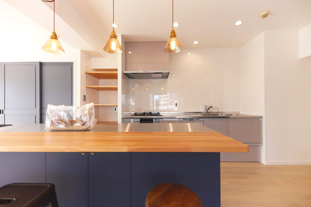 Inspiration for a large scandinavian single-wall open plan kitchen in Nagoya with an undermount sink, open cabinets, blue cabinets, stainless steel benchtops, white splashback, glass sheet splashback, coloured appliances, light hardwood floors, with island, white floor and grey benchtop.