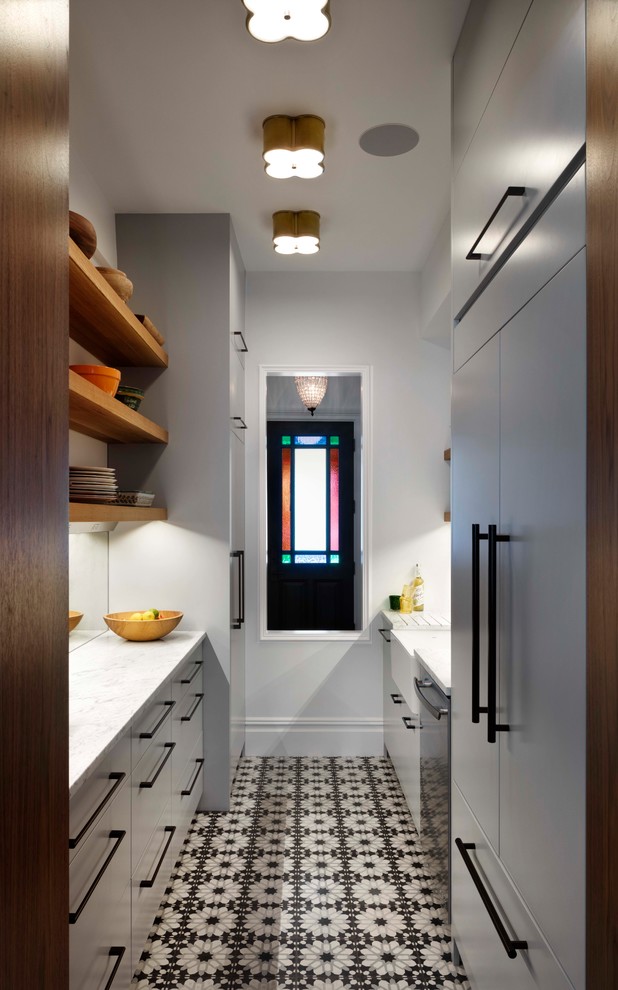 This is an example of a contemporary galley kitchen in Denver with a farmhouse sink, flat-panel cabinets, grey cabinets, white splashback, panelled appliances, no island, multi-coloured floor and white benchtop.