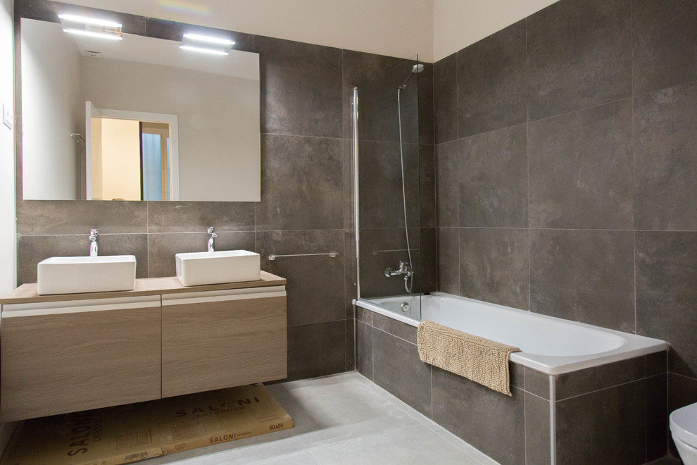 Photo of a large contemporary master bathroom in Madrid with furniture-like cabinets, grey cabinets, a curbless shower, a two-piece toilet, beige tile, porcelain tile, beige walls, porcelain floors, a vessel sink, laminate benchtops, beige floor and a sliding shower screen.