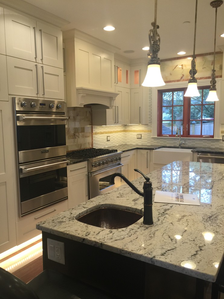 Eat-in kitchen - mid-sized transitional u-shaped light wood floor and beige floor eat-in kitchen idea in Boston with a farmhouse sink, granite countertops, stainless steel appliances, an island, recessed-panel cabinets, white cabinets, beige backsplash, stone tile backsplash and multicolored countertops