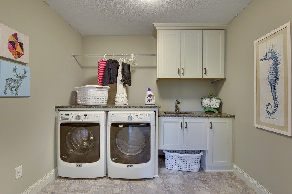 Photo of a large transitional single-wall dedicated laundry room in Minneapolis with an undermount sink, recessed-panel cabinets, white cabinets, grey walls, ceramic floors and a side-by-side washer and dryer.