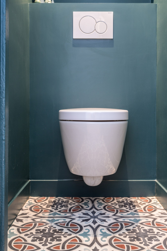 Inspiration for a small modern powder room in London with open cabinets, blue cabinets, a wall-mount toilet, blue walls, cement tiles, multi-coloured floor and white benchtops.