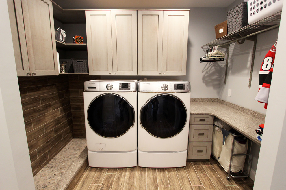 Photo of a mid-sized transitional galley utility room with flat-panel cabinets, grey cabinets, grey walls, laminate floors, a side-by-side washer and dryer and brown floor.