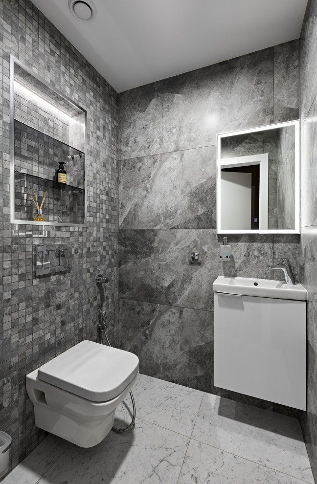 Photo of a medium sized contemporary cloakroom in Saint Petersburg with flat-panel cabinets, white cabinets, a wall mounted toilet, grey tiles, mosaic tiles, grey walls, porcelain flooring, a built-in sink, solid surface worktops, grey floors, white worktops and a floating vanity unit.
