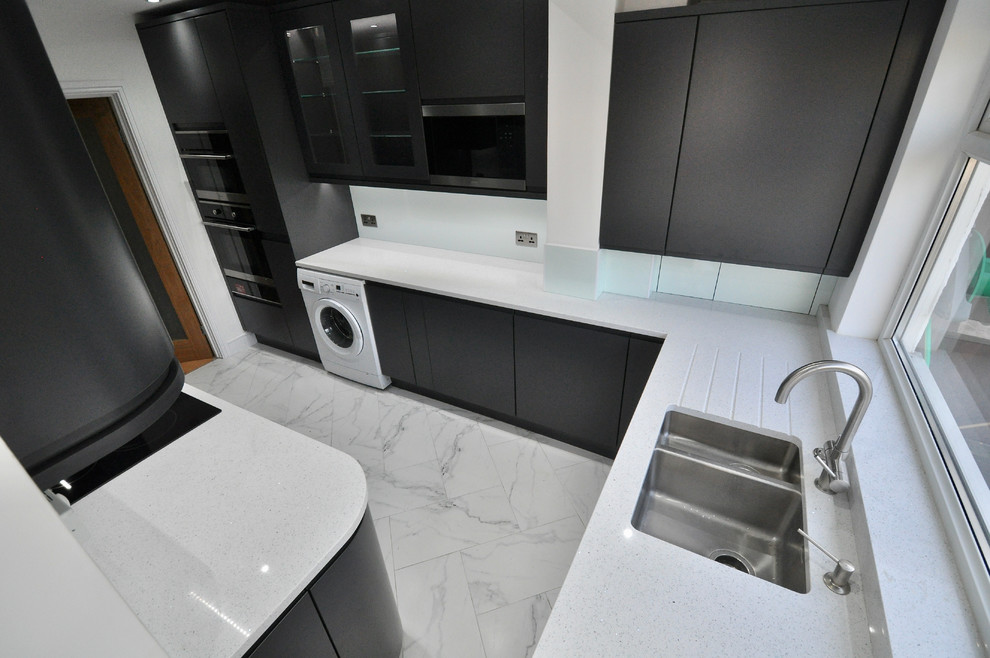 Mid-sized contemporary u-shaped separate kitchen in London with an integrated sink, flat-panel cabinets, grey cabinets, quartzite benchtops, green splashback, black appliances, porcelain floors, no island, white floor and white benchtop.