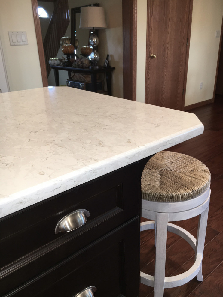 Example of a large transitional medium tone wood floor and brown floor home design design with an undermount sink, flat-panel cabinets, white cabinets, granite countertops, white backsplash, porcelain backsplash, stainless steel appliances and an island