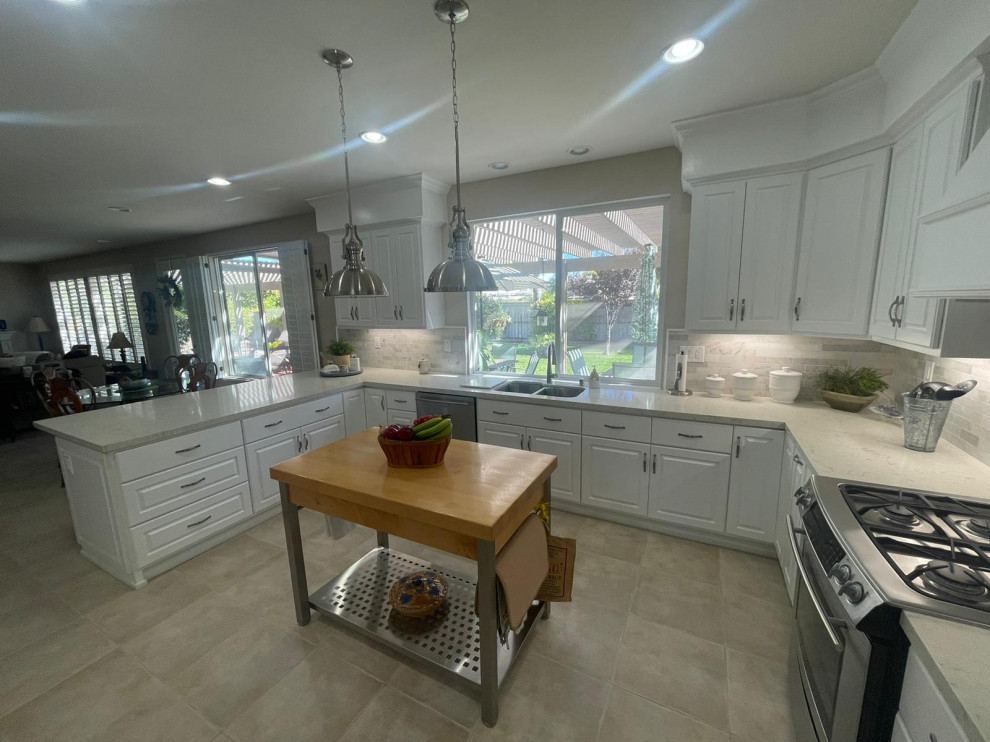 Large transitional u-shaped open plan kitchen in Los Angeles with a double-bowl sink, beaded inset cabinets, white cabinets, stainless steel appliances, ceramic floors, with island, beige floor and beige benchtop.