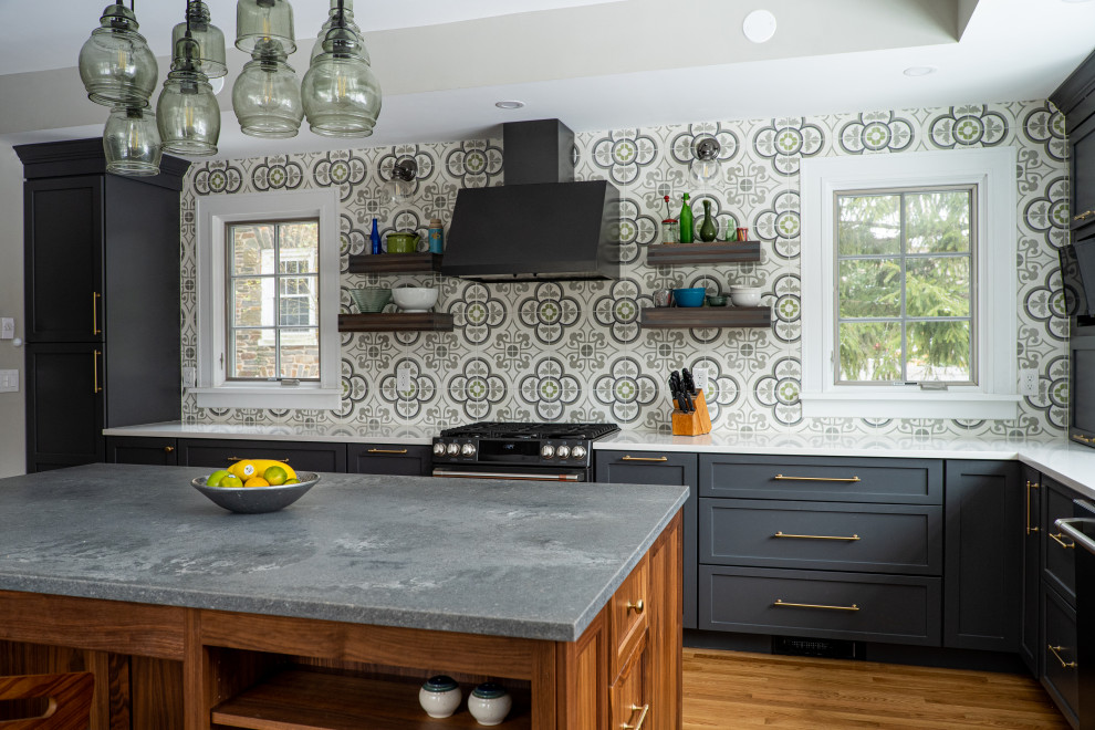 This is an example of a large midcentury l-shaped eat-in kitchen in Baltimore with a farmhouse sink, shaker cabinets, grey cabinets, soapstone benchtops, multi-coloured splashback, cement tile splashback, black appliances, medium hardwood floors, with island, brown floor, grey benchtop and recessed.