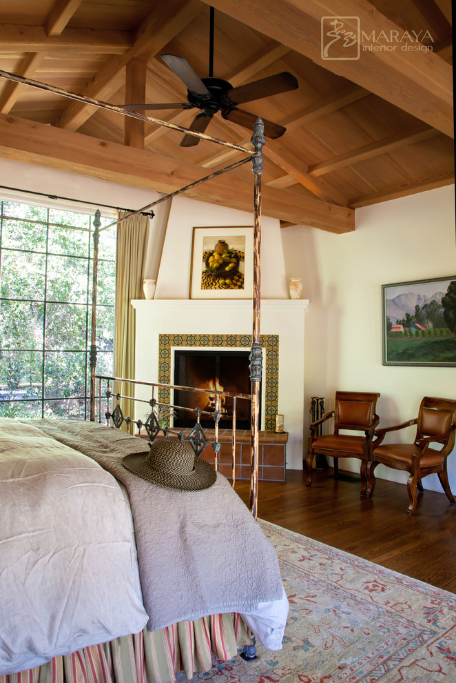 Design ideas for a large mediterranean master bedroom in Santa Barbara with white walls, medium hardwood floors, a corner fireplace and a tile fireplace surround.
