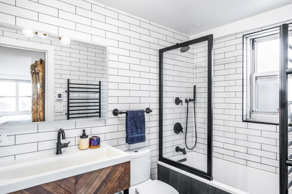 Foto på ett industriellt vit en-suite badrum, med ett platsbyggt badkar, en dusch/badkar-kombination, en toalettstol med separat cisternkåpa, vit kakel, porslinskakel, vita väggar, klinkergolv i porslin, ett avlångt handfat, bänkskiva i betong, svart golv och med dusch som är öppen