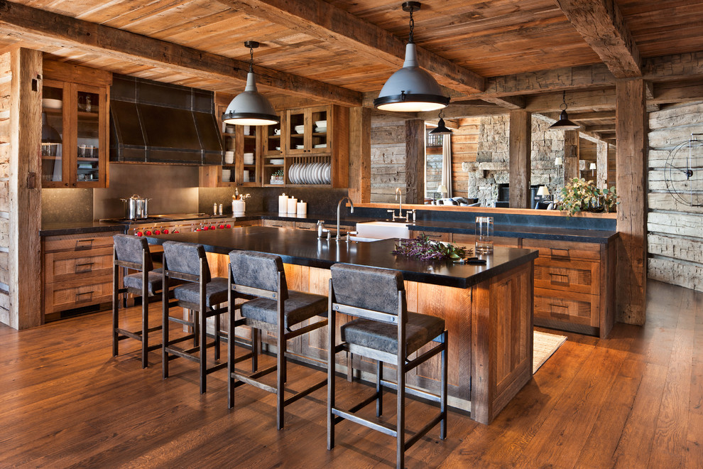 This is an example of a country l-shaped kitchen in Other with a farmhouse sink, glass-front cabinets, medium wood cabinets, metallic splashback, stainless steel appliances, medium hardwood floors, with island, brown floor and black benchtop.