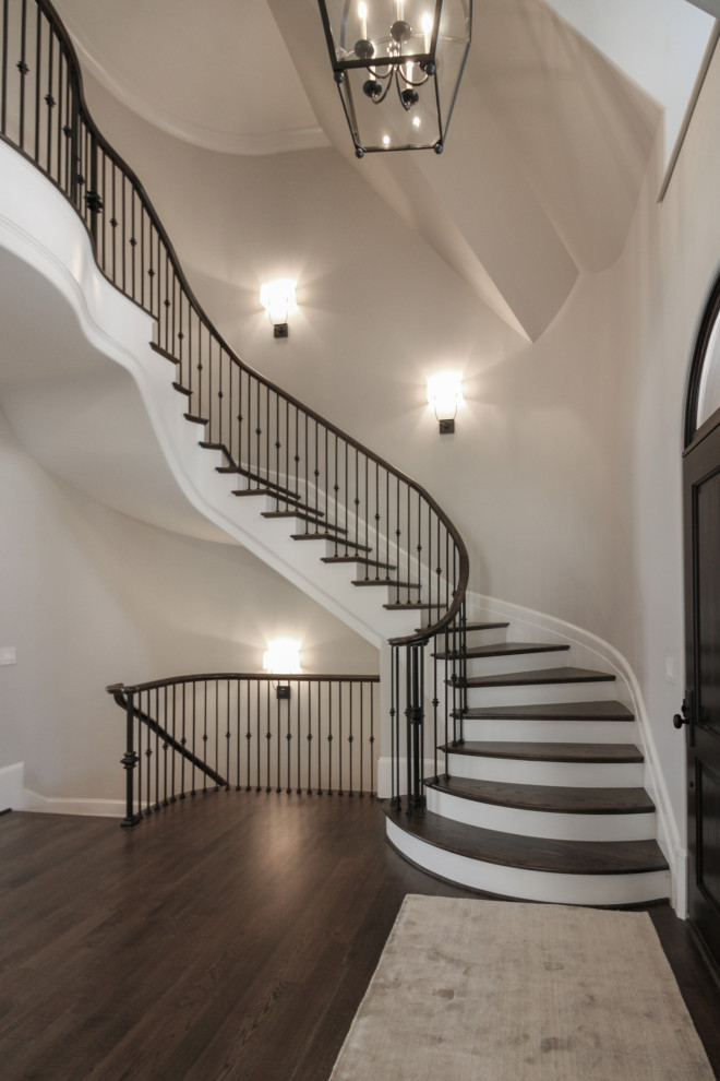 Стильный дизайн: большая лестница на больцах в классическом стиле с деревянными ступенями, крашенными деревянными подступенками и металлическими перилами - последний тренд