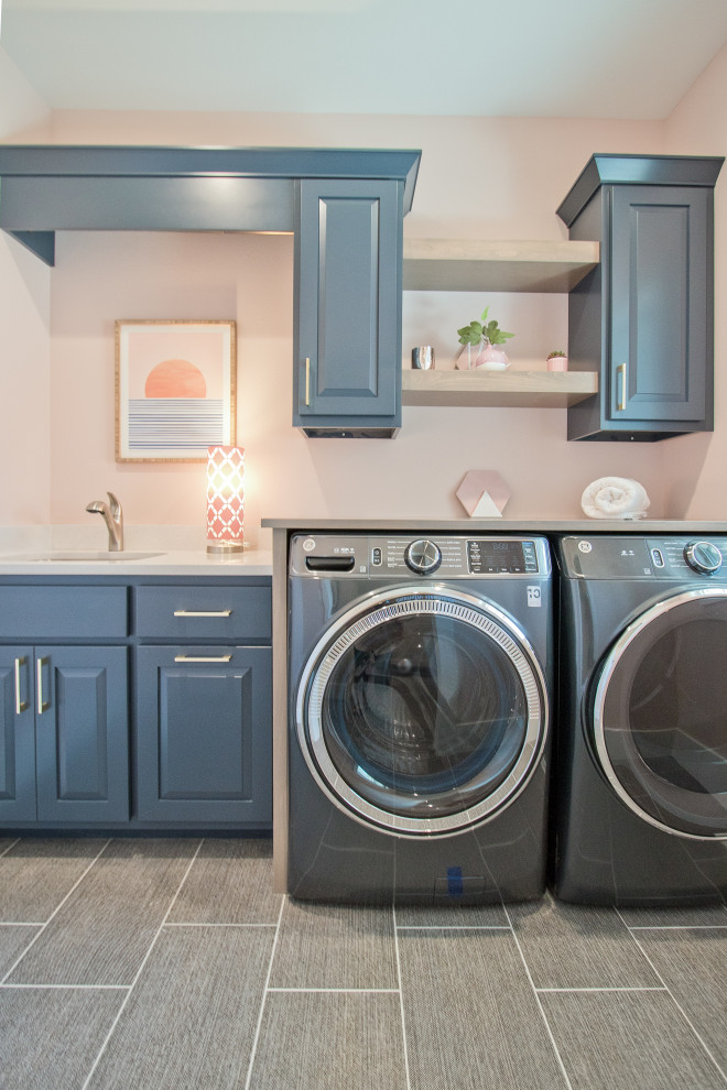 Transitional single-wall laundry room with an undermount sink, pink walls, vinyl floors, a side-by-side washer and dryer, white benchtop and brown floor.