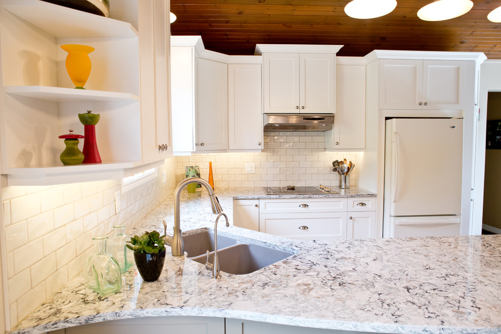 Example of a mid-sized transitional u-shaped light wood floor kitchen design in Toronto with an undermount sink, shaker cabinets, white cabinets, granite countertops, white backsplash, subway tile backsplash, white appliances and a peninsula