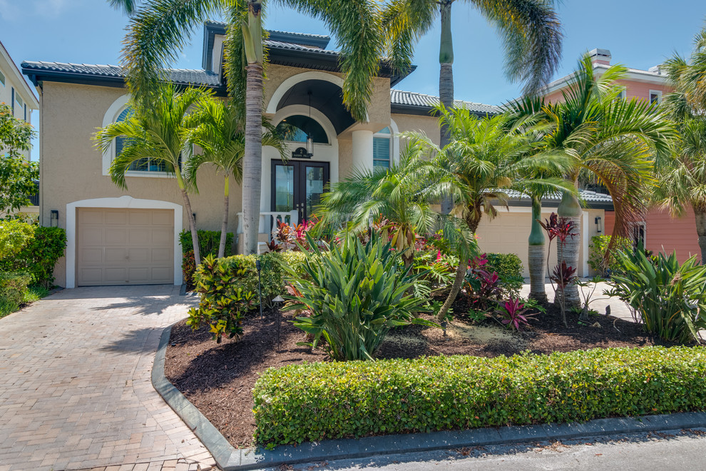 Photo of a large tropical three-storey stucco beige house exterior in Tampa with a hip roof and a tile roof.