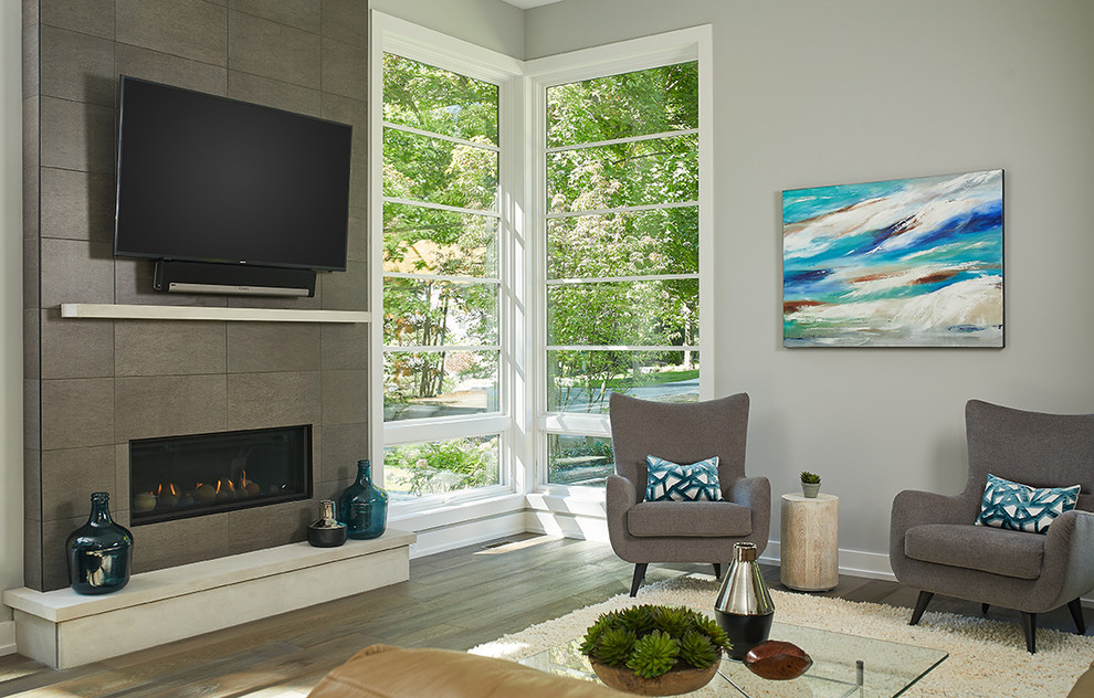 This is an example of a modern open concept living room in Grand Rapids with grey walls, medium hardwood floors, a standard fireplace, a metal fireplace surround, a wall-mounted tv and brown floor.