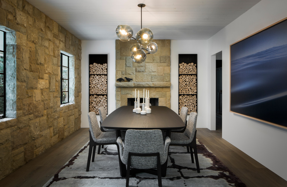 This is an example of a large transitional separate dining room in Santa Barbara with white walls, a standard fireplace, a stone fireplace surround, brown floor, medium hardwood floors and timber.