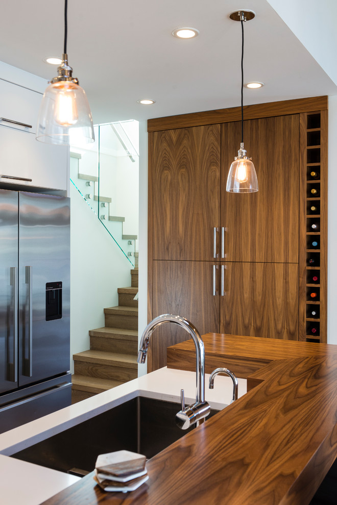 Mid-sized l-shaped light wood floor and brown floor open concept kitchen photo in Vancouver with an undermount sink, flat-panel cabinets, white cabinets, quartz countertops, white backsplash, ceramic backsplash, stainless steel appliances and an island