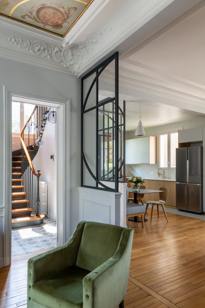 This is an example of a large grey and white open plan living room in Paris with a reading nook, grey walls, light hardwood flooring, a standard fireplace, a wall mounted tv, brown floors, a drop ceiling and wainscoting.