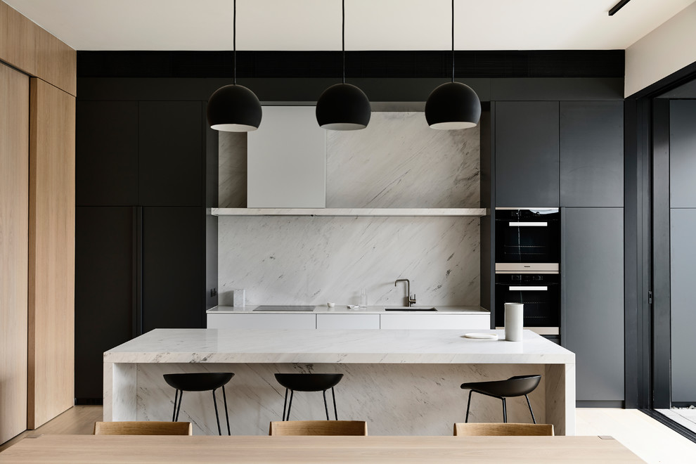 Photo of a contemporary galley kitchen in Melbourne with an undermount sink, flat-panel cabinets, black cabinets, white splashback, stone slab splashback, with island and white benchtop.