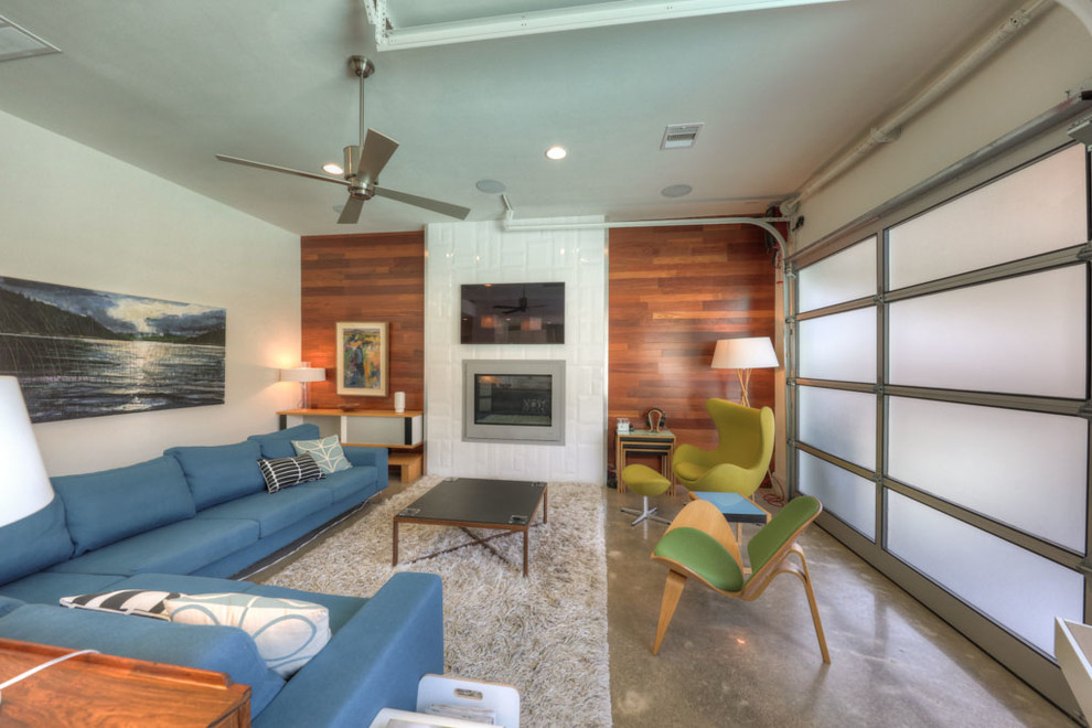 Photo of a large midcentury open concept family room in Houston with white walls, concrete floors, a standard fireplace, a tile fireplace surround, a wall-mounted tv and grey floor.