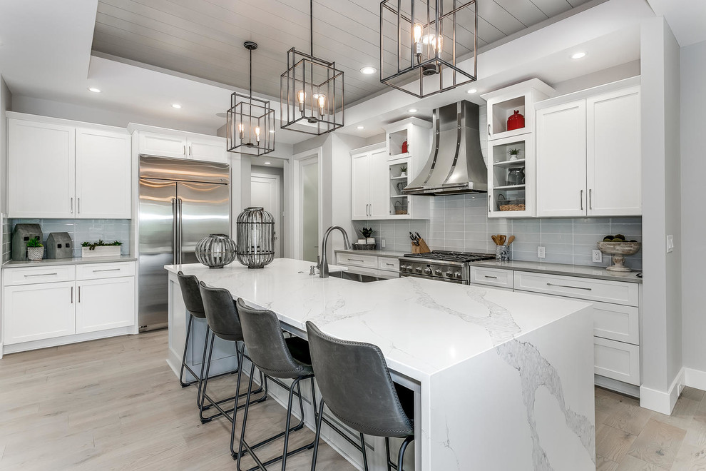 Inspiration for a large modern l-shaped eat-in kitchen in Wichita with a farmhouse sink, shaker cabinets, white cabinets, grey splashback, ceramic splashback, stainless steel appliances, light hardwood floors, with island, brown floor, grey benchtop and granite benchtops.