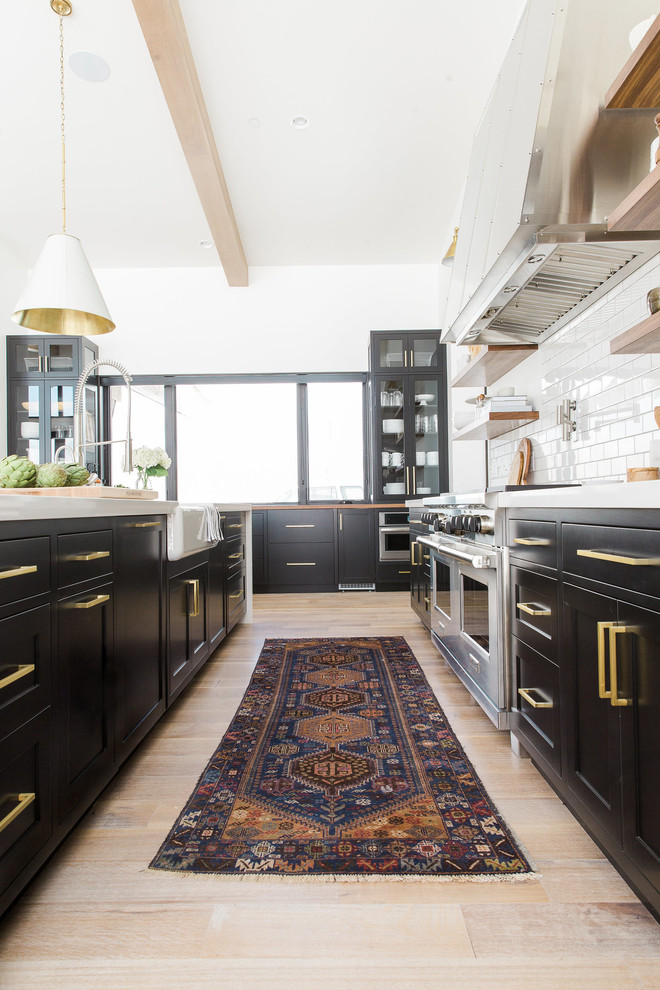Inspiration for a transitional l-shaped open plan kitchen in Salt Lake City with a drop-in sink, flat-panel cabinets, black cabinets, white splashback, subway tile splashback, stainless steel appliances, light hardwood floors and with island.