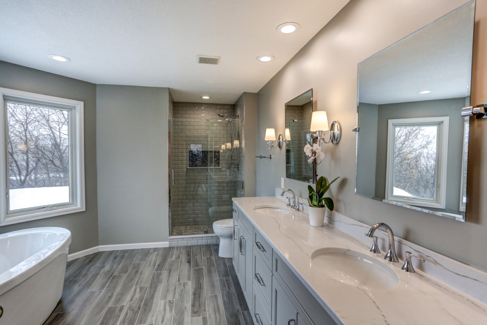 Large transitional master bathroom in Minneapolis with recessed-panel cabinets, grey cabinets, a freestanding tub, an alcove shower, a two-piece toilet, gray tile, grey walls, an undermount sink, engineered quartz benchtops, grey floor, grey benchtops, subway tile, porcelain floors and a hinged shower door.
