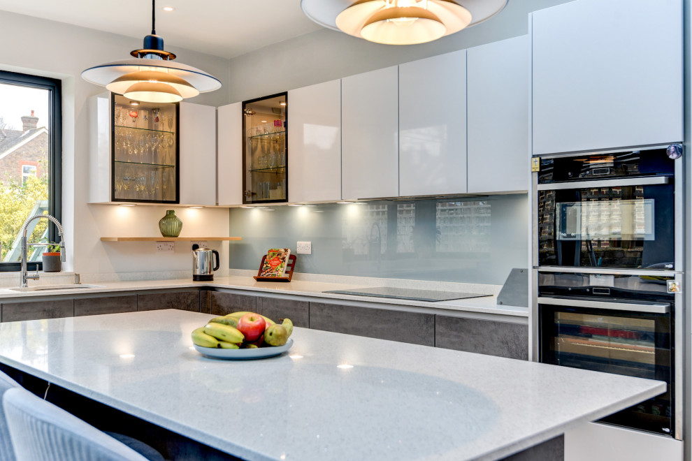 Mid-sized modern l-shaped eat-in kitchen in Sussex with an undermount sink, flat-panel cabinets, grey cabinets, granite benchtops, blue splashback, glass sheet splashback, panelled appliances, light hardwood floors, with island, brown floor and white benchtop.