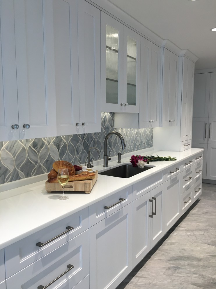 Photo of an expansive contemporary u-shaped eat-in kitchen in New York with a single-bowl sink, shaker cabinets, white cabinets, quartzite benchtops, grey splashback, glass sheet splashback, stainless steel appliances, ceramic floors and multiple islands.