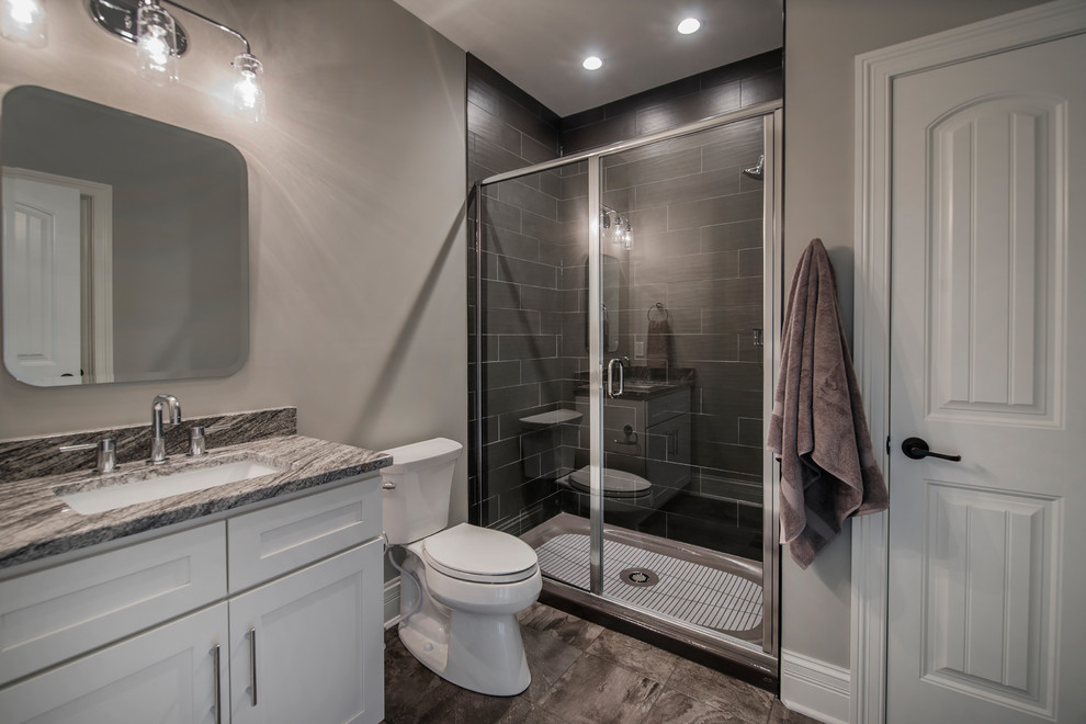 This is an example of a mid-sized traditional bathroom in Columbus with flat-panel cabinets, white cabinets, a two-piece toilet, black tile, porcelain tile, grey walls, porcelain floors, an undermount sink, granite benchtops, grey floor and a hinged shower door.