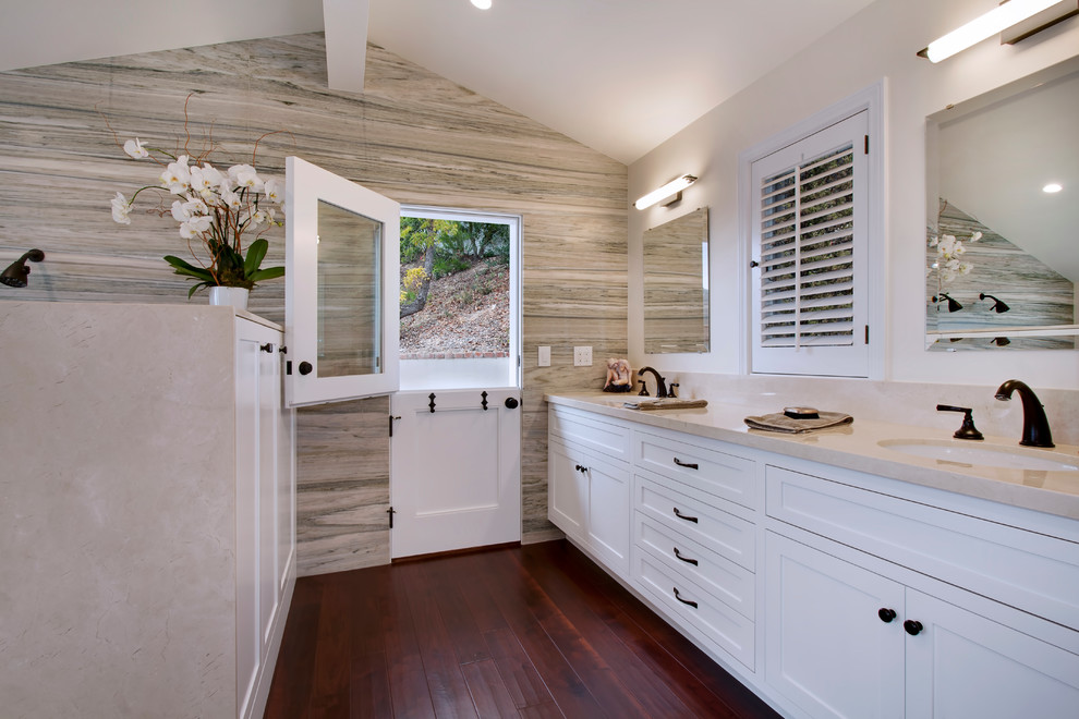 This is an example of a large arts and crafts master bathroom in Los Angeles with an undermount sink, shaker cabinets, white cabinets, marble benchtops, a claw-foot tub, an open shower, a two-piece toilet, stone tile, white walls, dark hardwood floors, beige tile, brown floor and an open shower.